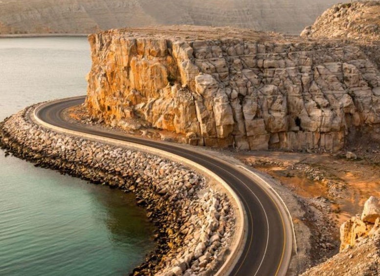 A winding road along a rocky coastline with a large cliff formation. 3