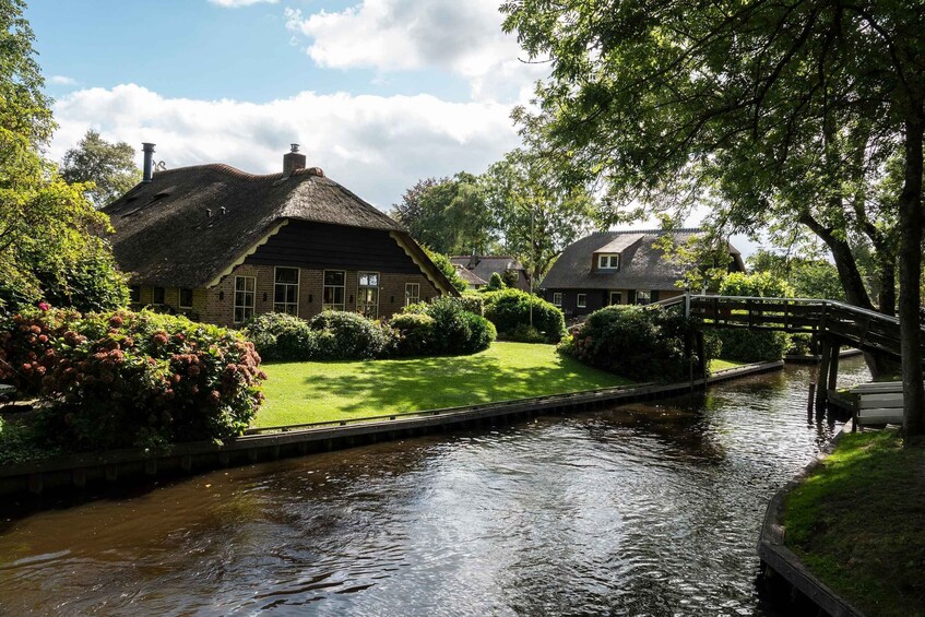 A traditional thatched-roof house with a canal, a wooden bridge, and lush greenery. 2