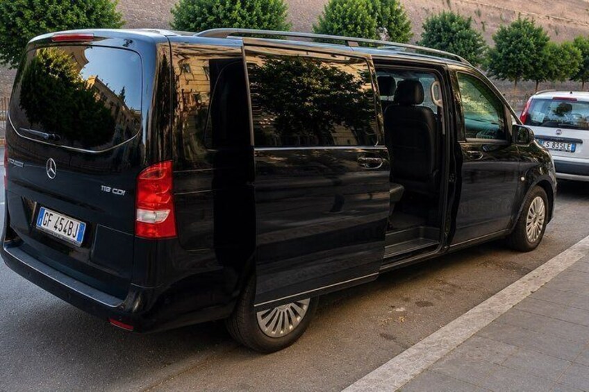 A black Mercedes-Benz Sprinter van parked on a street with trees and a building in the background. 3