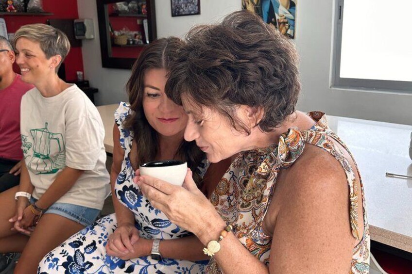 A person holding a white cup, seated indoors with another person. 5