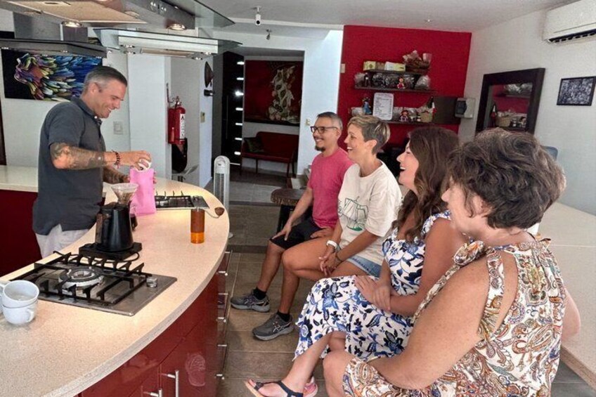 A group of people sitting around a bar area with a man pouring a drink. 1