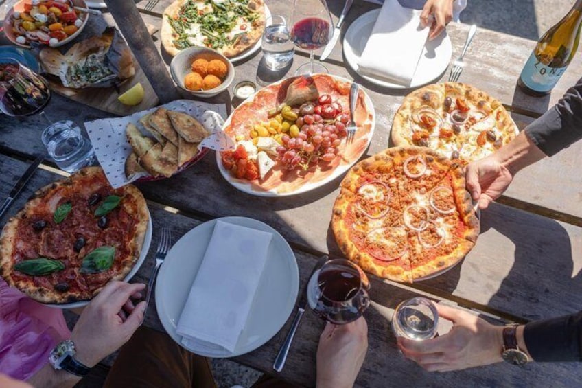A group of people around a table with various pizzas and drinks. 1