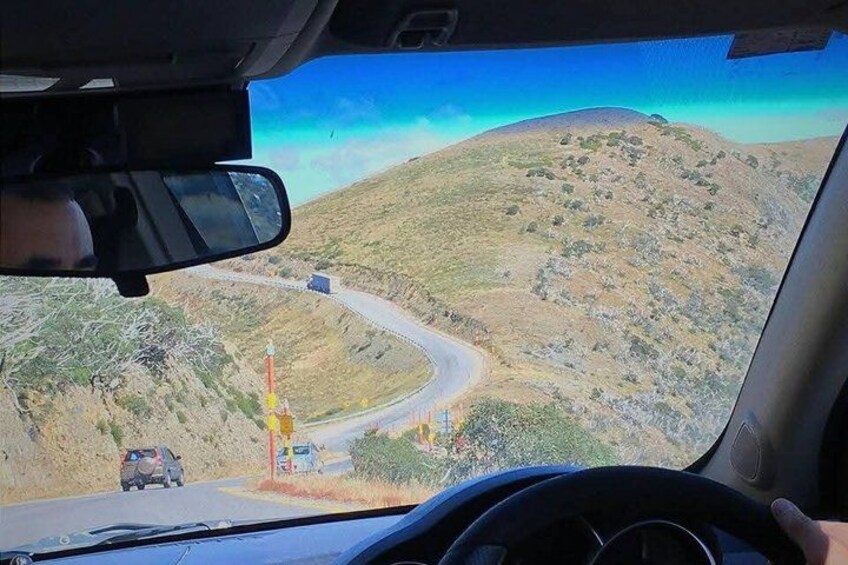 A winding road on a hilly landscape with a vehicle in the foreground and a distant truck on the road. 3