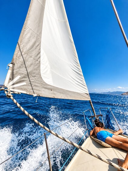 A sailboat with a person lying on a sunshade, the ocean, and a clear blue sky. 4