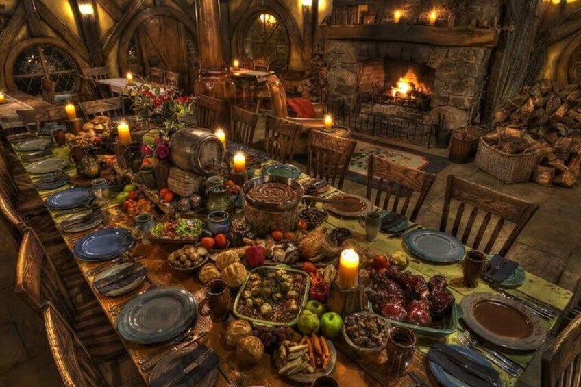 A long wooden table set for a feast with various dishes, candles, and a roaring fireplace in the background. 4