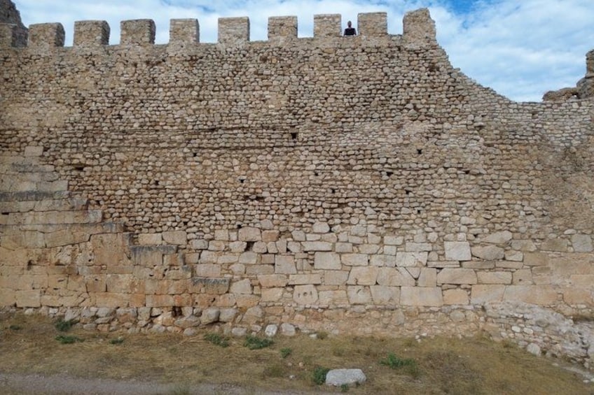 A stone wall with a crenellated top and a person standing on it. 3