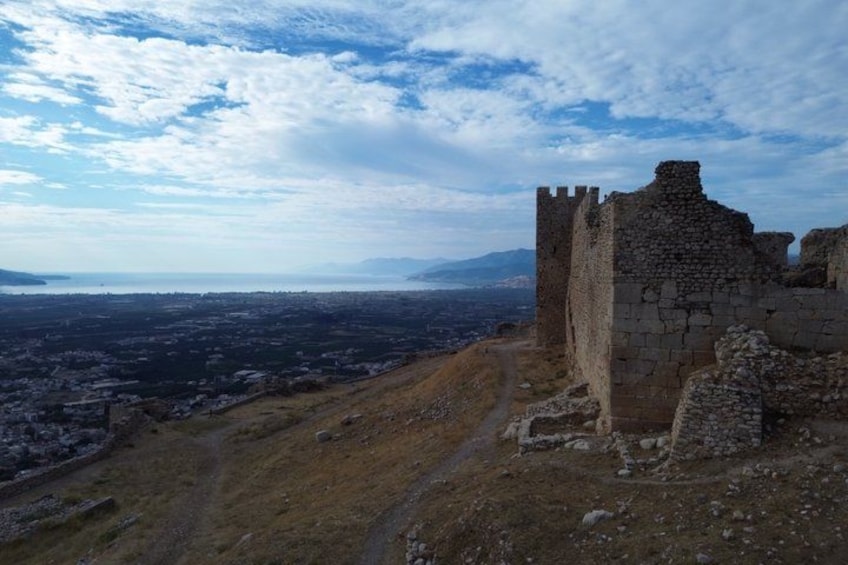 A historical stone structure with a tower, overlooking a city and distant mountains. 4