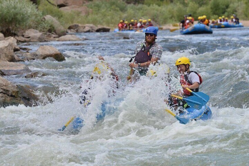 Two people in a blue raft navigating a river with waves. 2