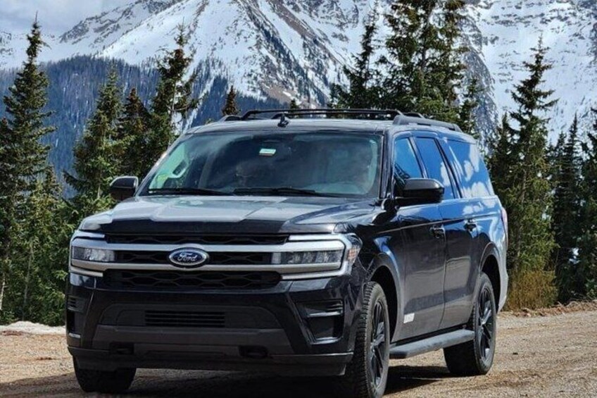 A black SUV parked on a dirt road with snow-capped mountains and evergreen trees in the background. 3