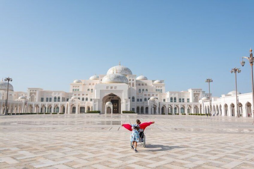 A large white building with domes, a tiled courtyard, and a person with a red umbrella. 5