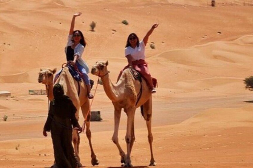 Two people riding camels in a desert landscape. 2