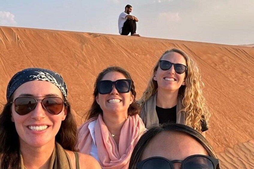 Three people on a sand dune with a person in the background. 5