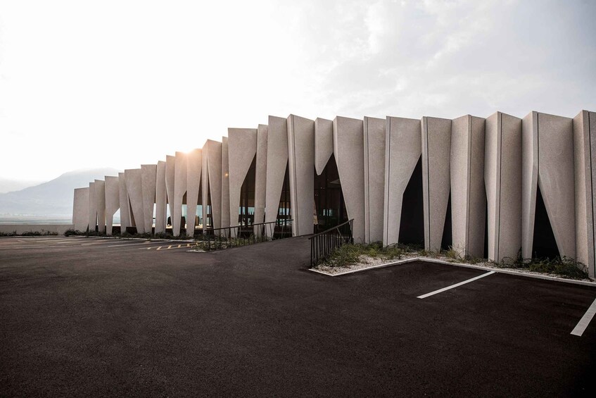 A modern architectural structure with a series of vertical concrete pillars and arched openings. 2