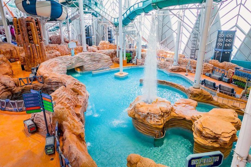 An indoor water park with a large pool, rock formations, and a water slide. 2