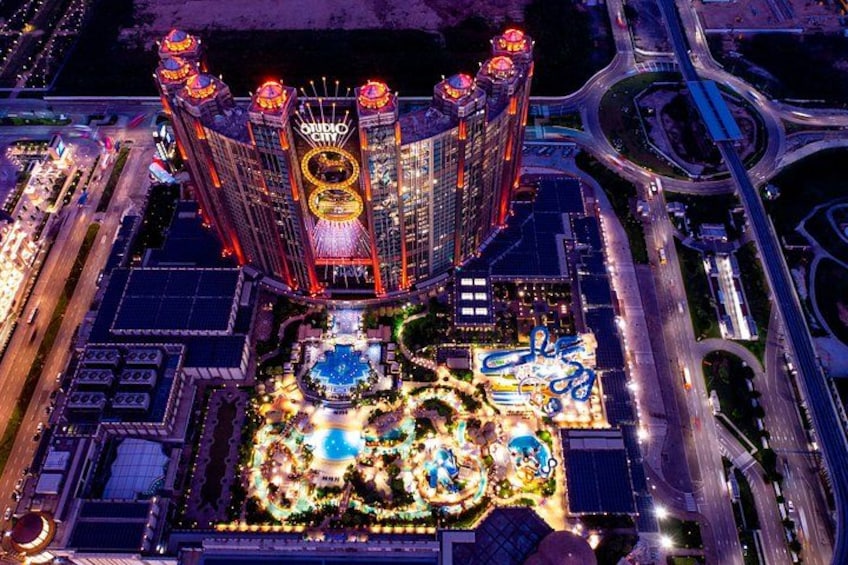 A brightly lit casino complex with a central fountain and surrounding buildings. 3