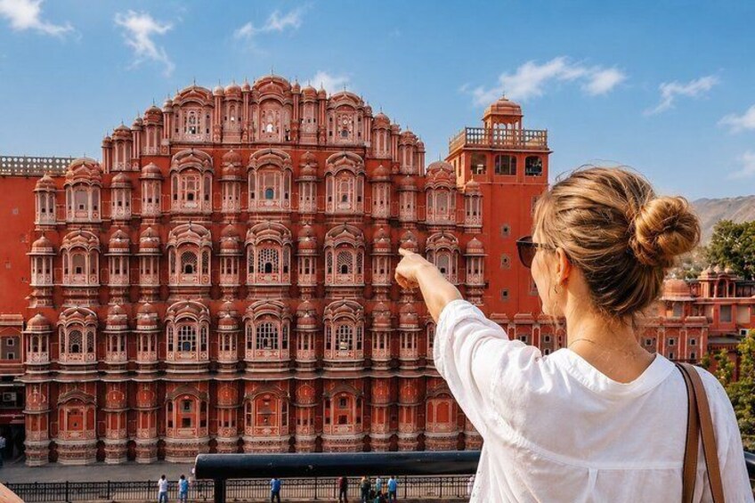 A woman pointing at a large, ornate building with multiple arches and windows. 1
