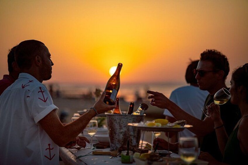 A sunset with people dining at a table by the beach. 1