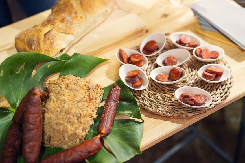 A wooden table with a loaf of bread, a bowl of food, and several small bowls containing slices of cured meat. 2