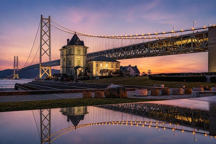 Un puente colgante, un edificio histórico y una masa de agua tranquila que refleja las estructuras. 1