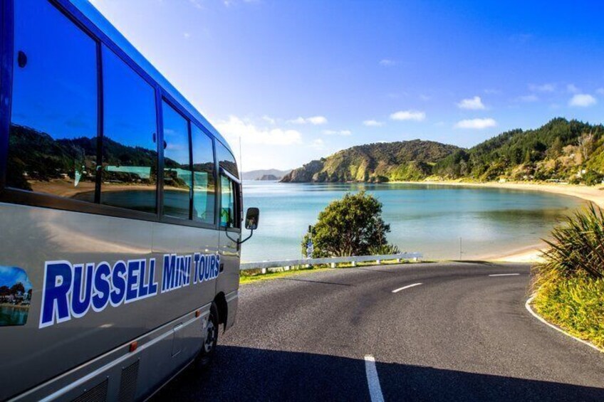 A bus with 'Russell Mini Tours' written on it parked by a scenic coastal road. 1