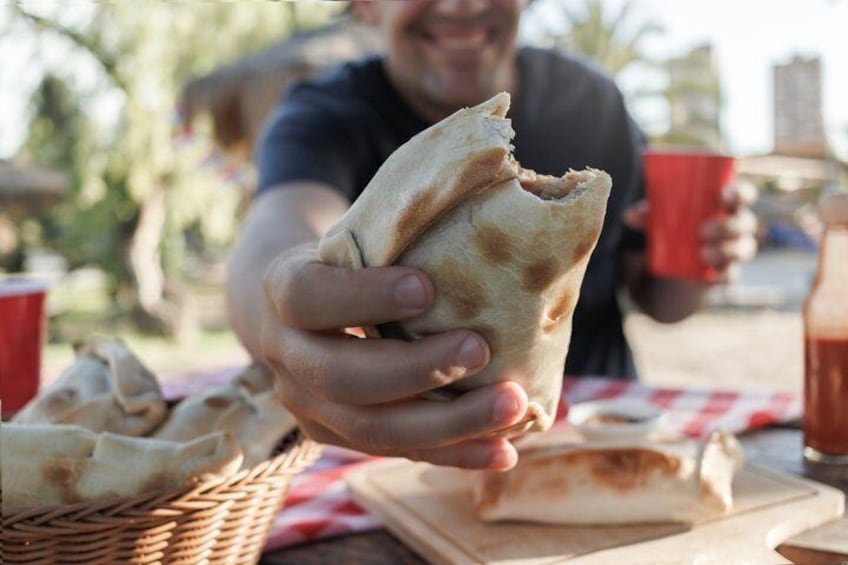 A person holding a pita bread, with a red cup and a basket of pita bread on a table. 1
