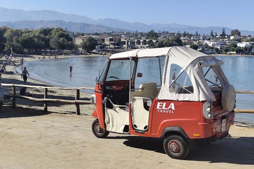 A red and white auto-rickshaw parked by a lake with a wooden walkway. 1