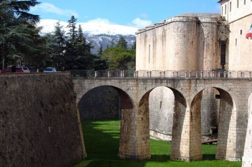 A stone bridge with arches, a stone wall, and a building in the background. 5