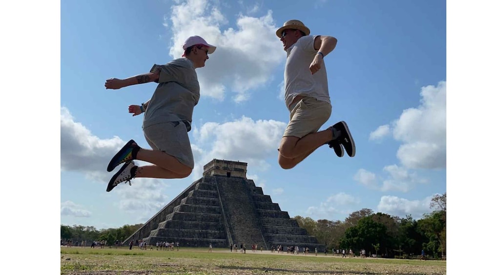 Two people jumping in front of a pyramid. 1