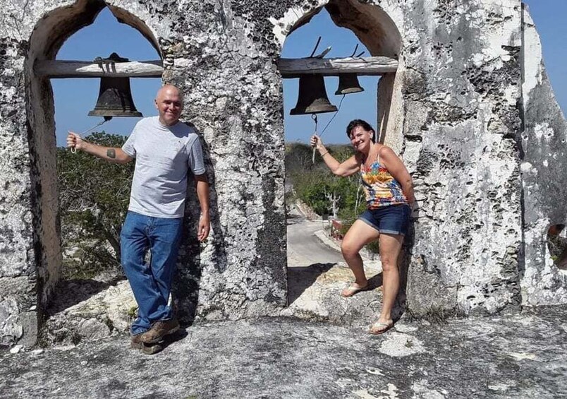 Two people standing in front of a stone structure with bell-shaped openings. 3