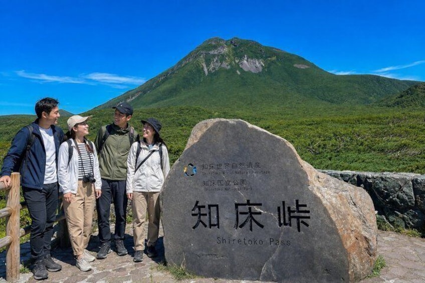 A group of hikers standing in front of a large rock with inscriptions, with a mountain in the background. 3