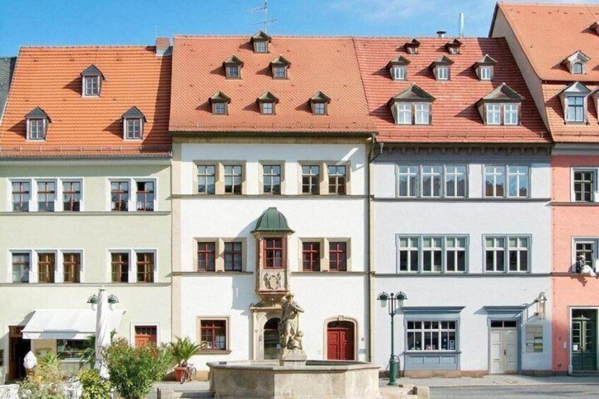 A row of colorful buildings with red-tiled roofs and a central fountain. 5