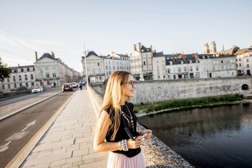A woman standing on a riverside walkway with buildings in the background. 3
