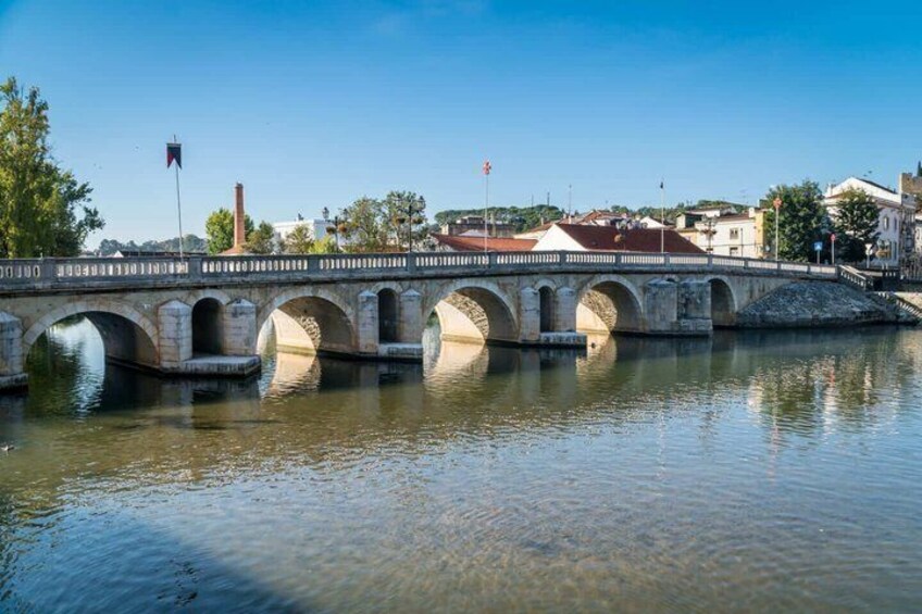 A stone bridge over a river with buildings and flags in the background. 2