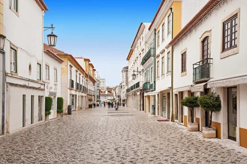 A cobblestone street lined with buildings, a clear sky, and a few pedestrians. 3