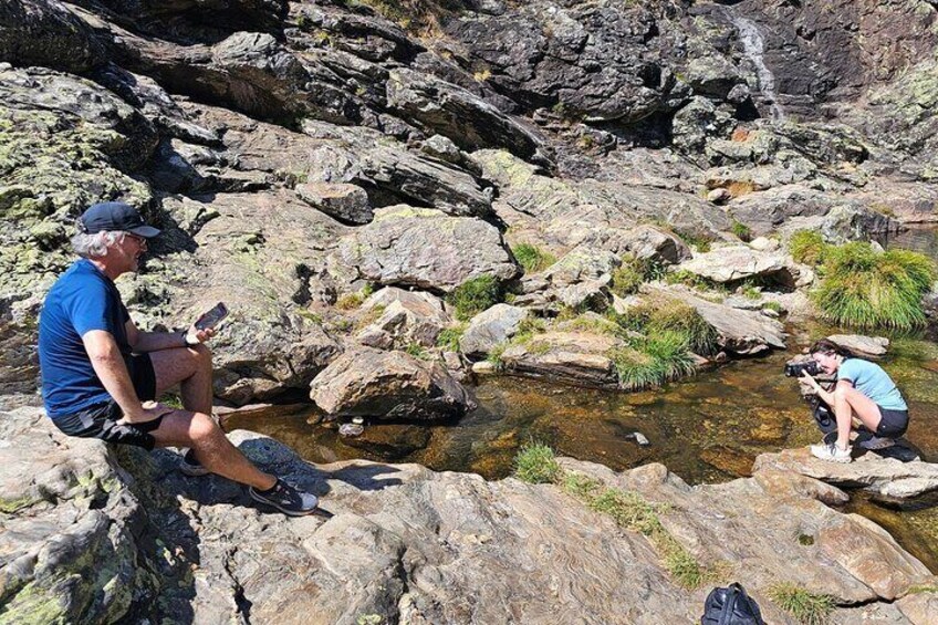 Two people sitting on rocks by a stream in a rocky terrain. 3