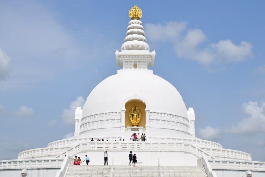 A white stupa with a golden spire, surrounded by steps and a clear sky. 4