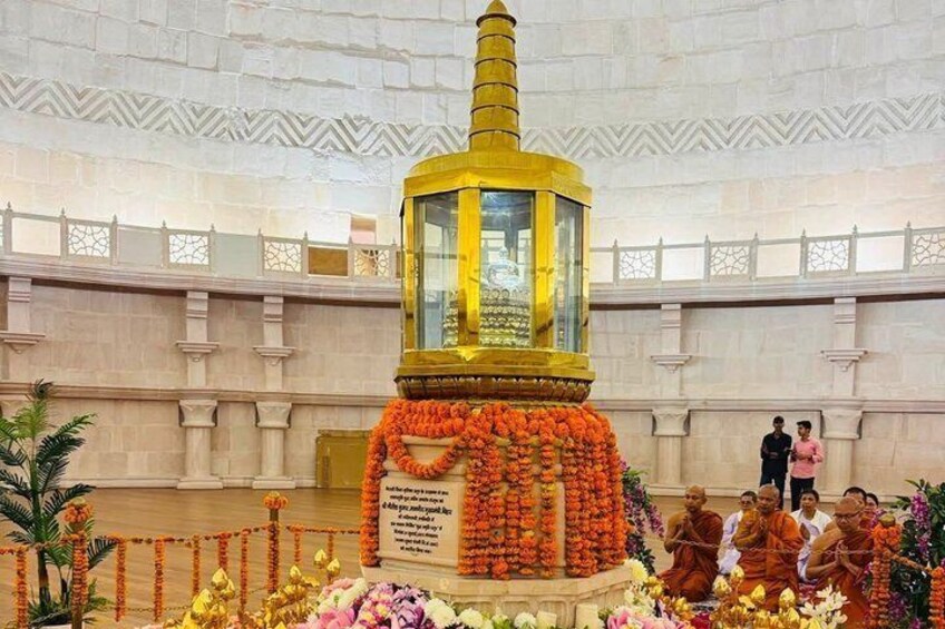 A golden stupa surrounded by flowers, with monks in traditional robes, set against a white marble background. 3