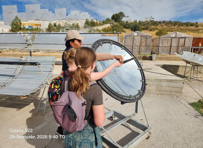 A solar panel installation with a large circular mirror and a person pointing at it. 3