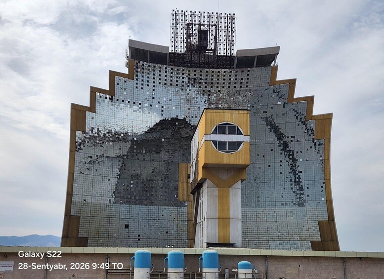 A large, uniquely designed building with a mosaic of reflective tiles, a prominent yellow and white section, and a metal framework at the top. 4