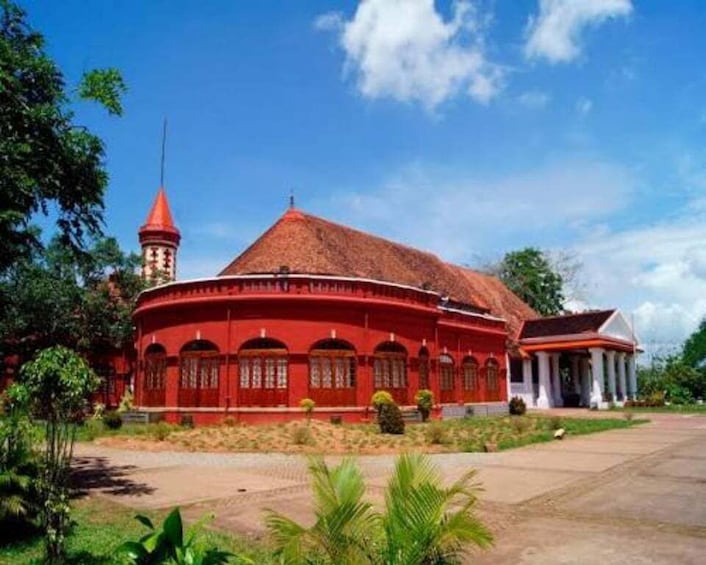 A red building with a thatched roof, a tower, and a smaller structure with columns. 1