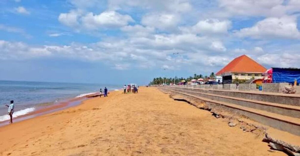 A sandy beach with a few people, a building with a red roof, and a clear sky. 3