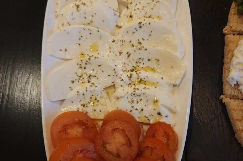 A white plate with sliced tomatoes and mozzarella cheese, garnished with herbs and olive oil. 5