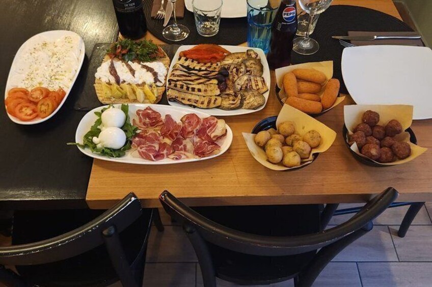 A table with various food items including a plate of sliced meats, a bowl of potatoes, and a dish with grilled vegetables. 1