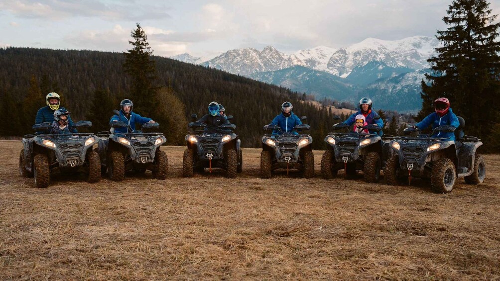 A group of people on ATVs in a grassy field with mountains in the background. 1