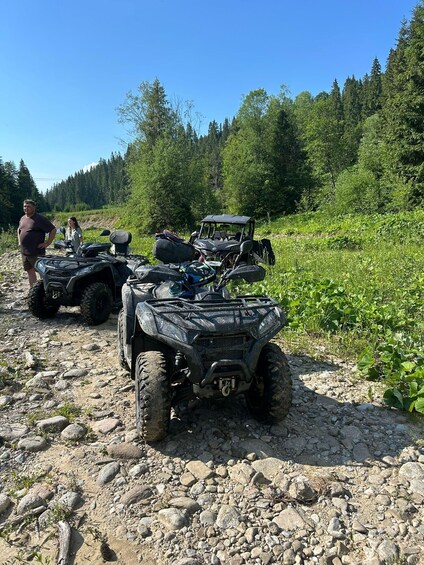 Off-road ATVs parked on a rocky trail with dense forest in the background. 2