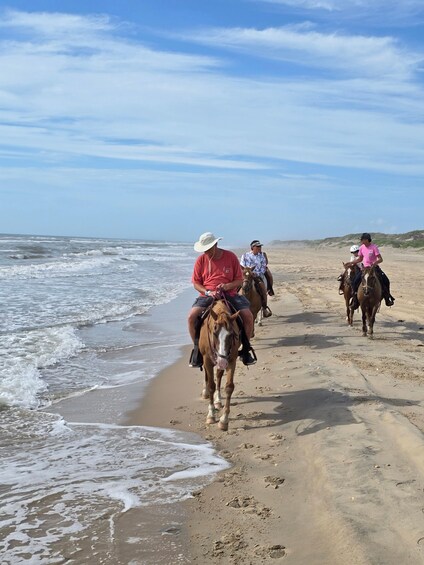 People riding horses along a sandy beach with waves crashing onto the shore. 5