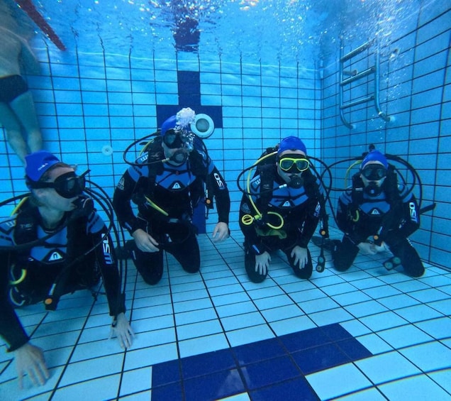 Four scuba divers in a pool with tiled walls and a ladder. 4