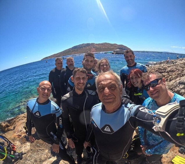 A group of people in wetsuits by a rocky coastline with clear blue water and a distant mountain. 2
