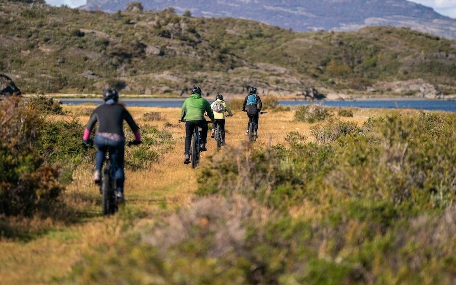 A group of cyclists on a trail with a lake and hills in the background. 4