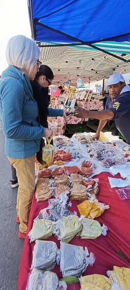 A market stall with various packaged goods spread out on a red cloth. 2